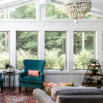 White, open Hudson, OH sunroom with blue lounge chairs, white beaded chandelier, and gray sofa Lindsey Putzier Design Studio