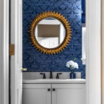Dark blue damask wallpaper, antiqued gold leaf round mirror, and brass vanity sconce Lindsey Putzier Design Studio