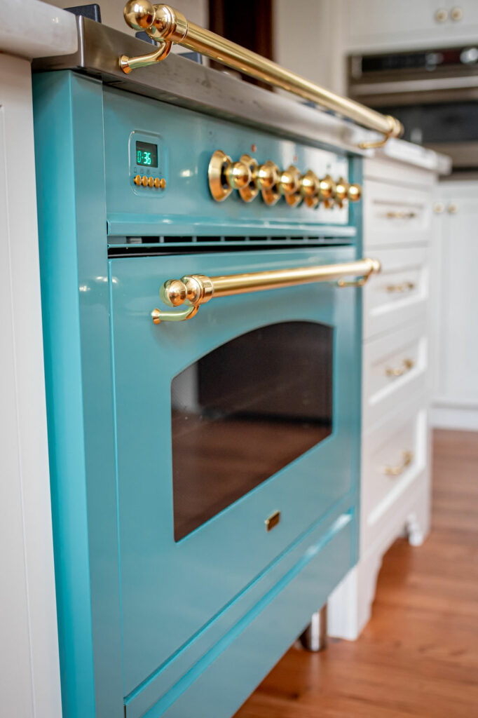 Teal European stove range beside white cabinetry with golden hardware Lindsey Putzier Design Studio