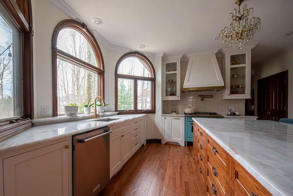 White cabinets, wooden floor, bay window, and teal oven range in Kitchen Design Lindsey Putzier Design Studio