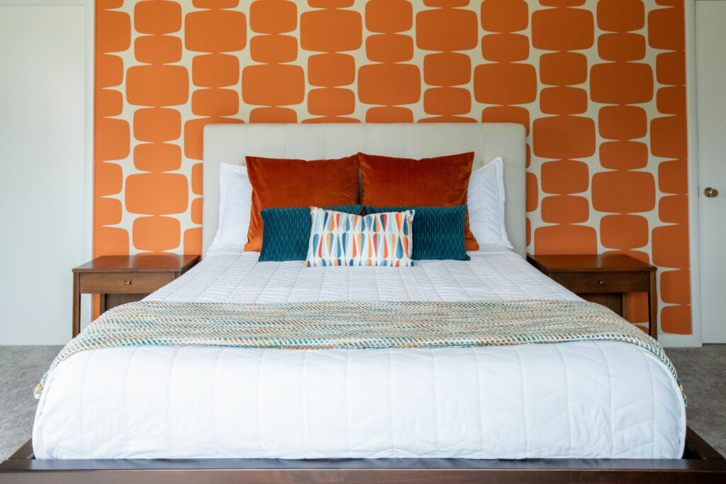 Patterned orange and white wallpapered accent wall with custom bed and vintage end tables Lindsey Putzier Design Studio Ohio