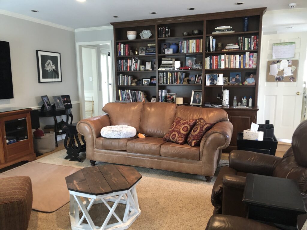 Before photo with brown leather sofa, dark brown bookshelves, and a brown rug