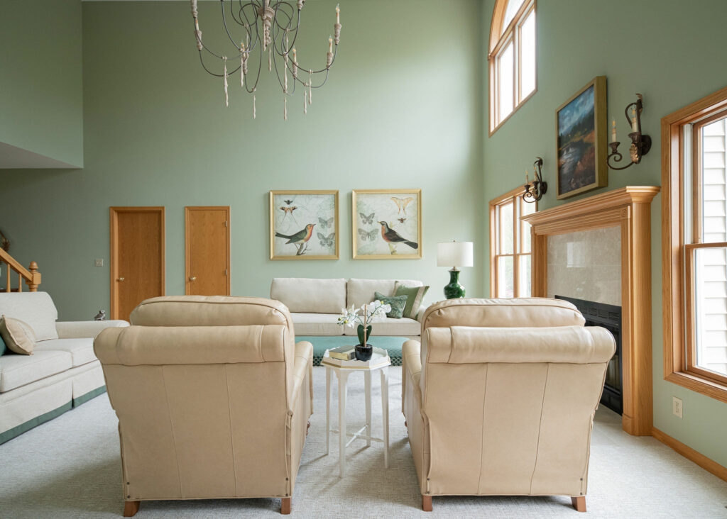 Family Room design with reupholstered sofa, leather recliners, softened green paint, and large white chandelier. Lindsey Putzier Design Studio
