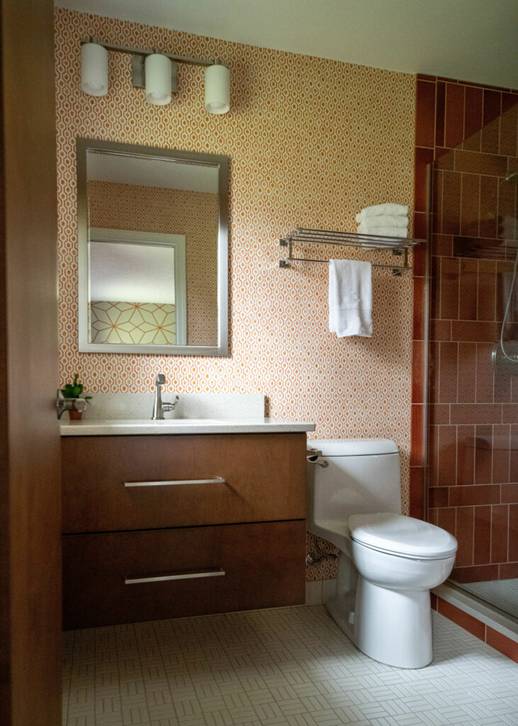 Orange patterned wallpaper and glass shower door in Bathroom design Lindsey Putzier Design Studio Ohio