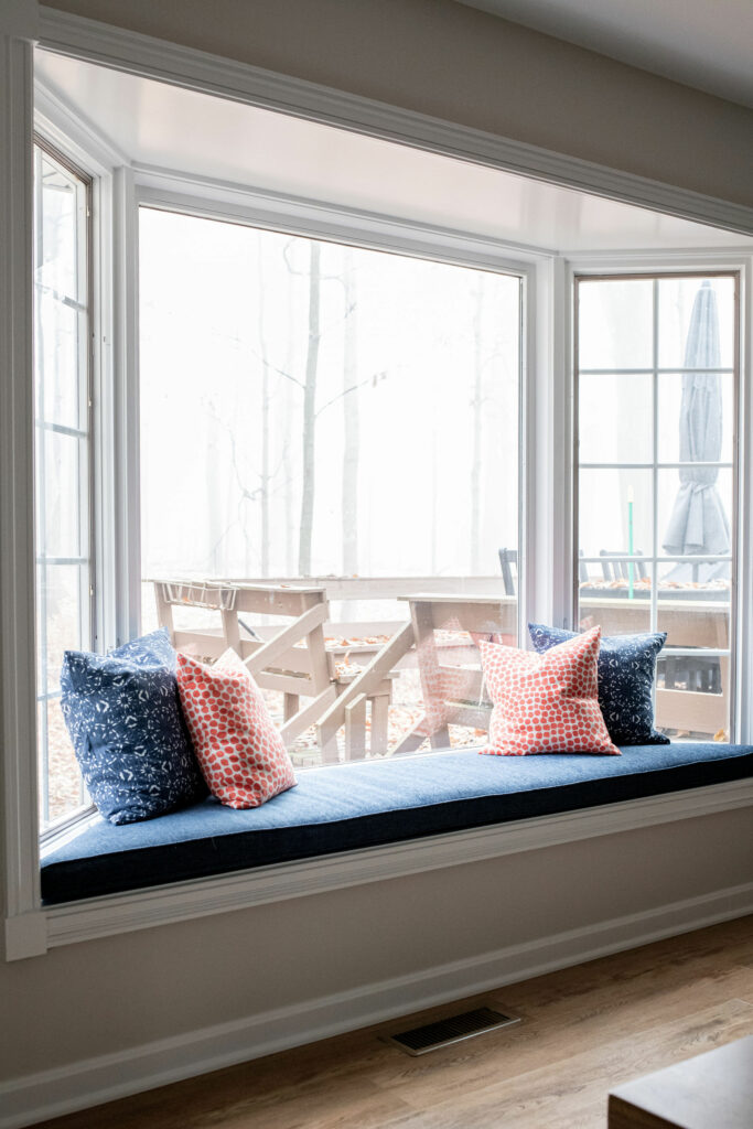 Updated bay window with blue window seat cushion and custom red and blue pillows in Dining Room design. Lindsey Putzier Design Studio