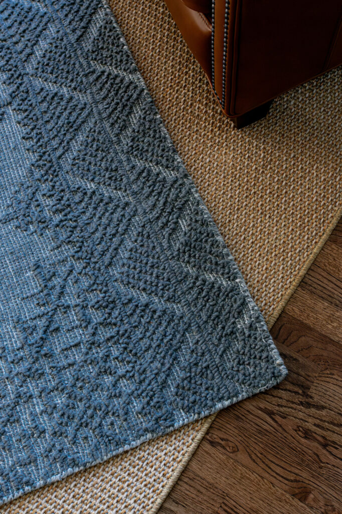Close up view of the layering of a custom size natural woven rug underneath the blue textured rug. Lindsey Putzier Design Studio, Hudson, Ohio