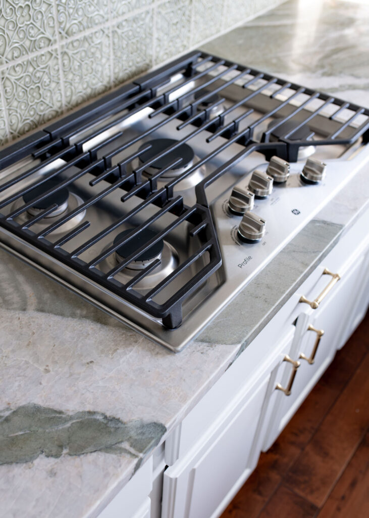 Gas stovetop in the Aurora Ohio Kitchen remodel with earthy green countertops and white cabinets. Lindsey Putzier interior design