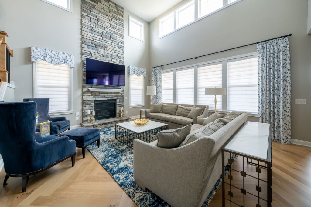 Living room with custom window treatments, stone fireplace, blue accents and sleek furniture. Brecksville Ohio interior Design Lindsey Putzier