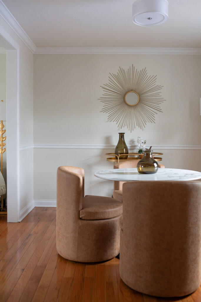 After of the dining room with marble tabletop, leather chairs, a golden bar cart and golden mirror on the wall. Parma Ohio interior design Lindsey Putzier