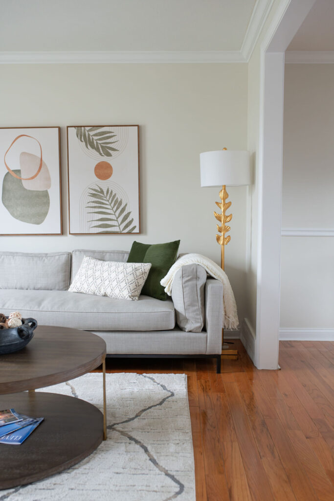 Golden lamp in the living room next to grey sofa with hardwood flooring. Parma Ohio interior design Lindsey Putzier