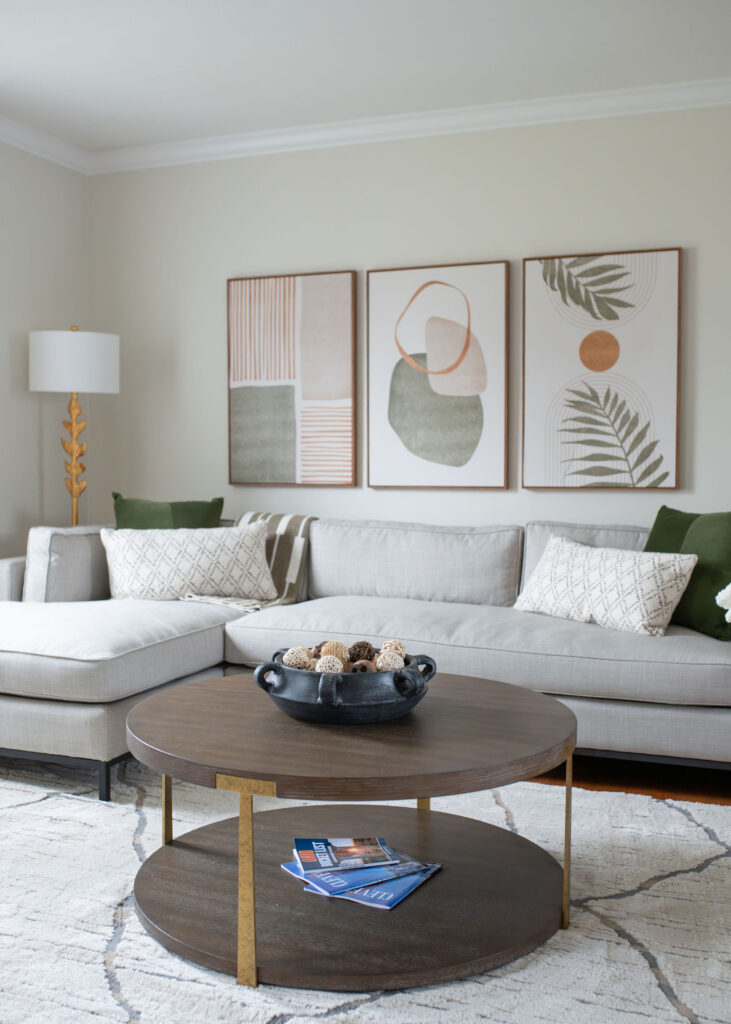 Sectional in the living room with patterned and green pillows, wooden coffee table and soft abstract art hanging on the walls. Parma Ohio interior design Lindsey Putzier