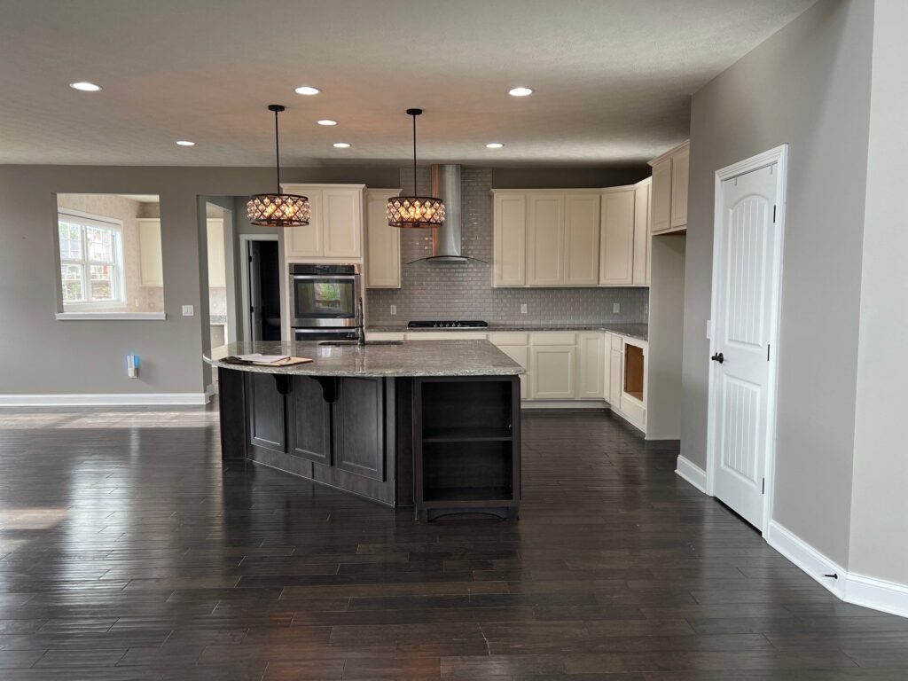  Before photo of the kitchen with dated white cabinets, pendant light fixtures, and dark hardwood flooring. Brecksville Ohio interior design Lindsey Putzier 