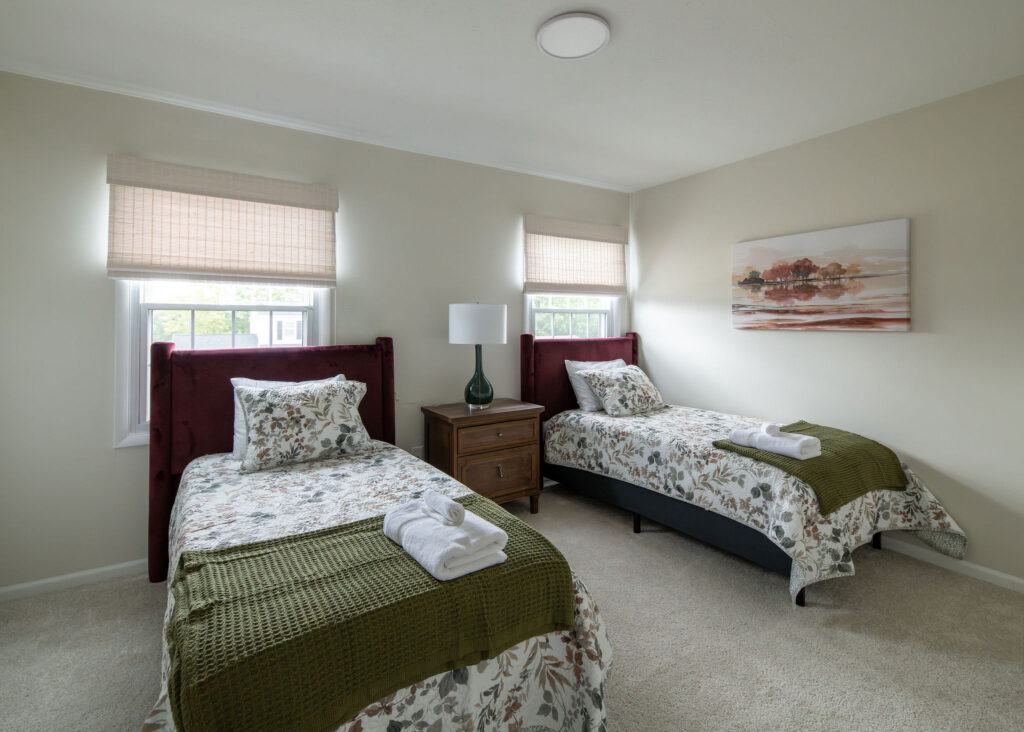 Secondary bedroom with two twin beds, deep red headboards, and earthy accents. Parma Ohio Vacation rentals Lindsey Putzier interior design