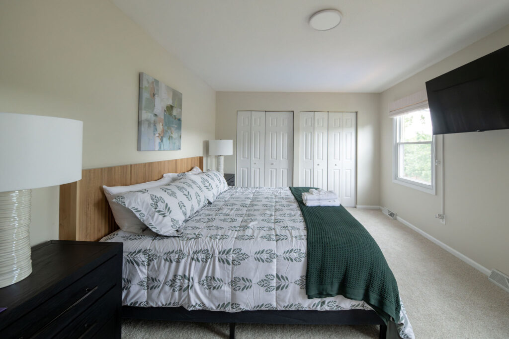 Master bedroom with cream walls and flooring, wooden headboard, and earth tone colors. Parma Ohio vacation rentals interior design Lindsey Putzier