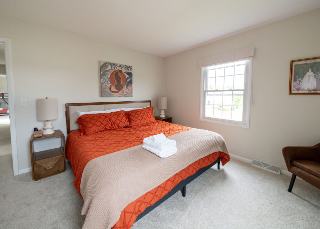 Secondary bedroom with bold burnt orange comforter and artwork. Lindsey Putzier interior design Parma Ohio vacation rental
