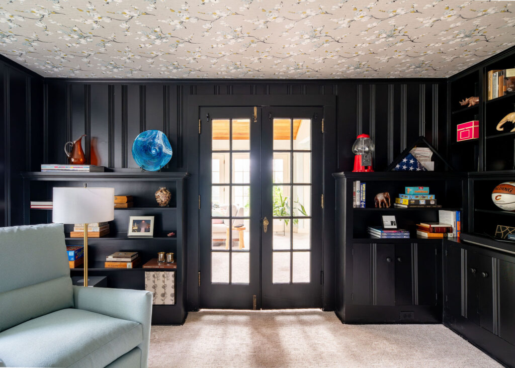 After design photo of Study in Hudson Ohio with wallpaper ceiling, many trinkets on the shelves and blue reading chairs