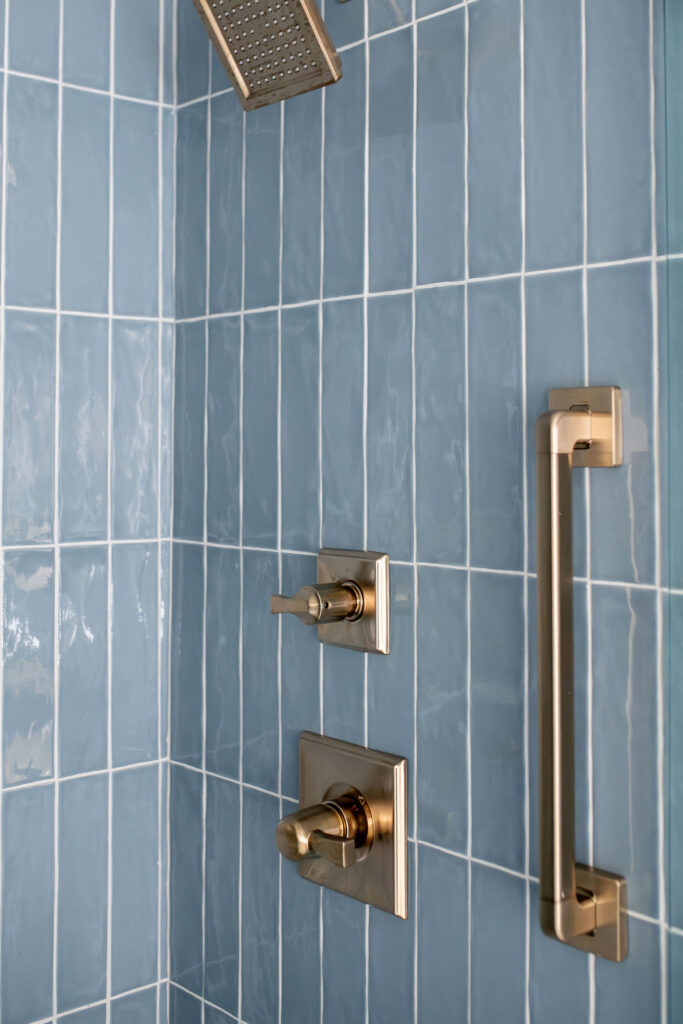 Glossy blue tiled shower in the master bathroom with golden hardware. Lindsey Putzier interior design Peninsula Ohio