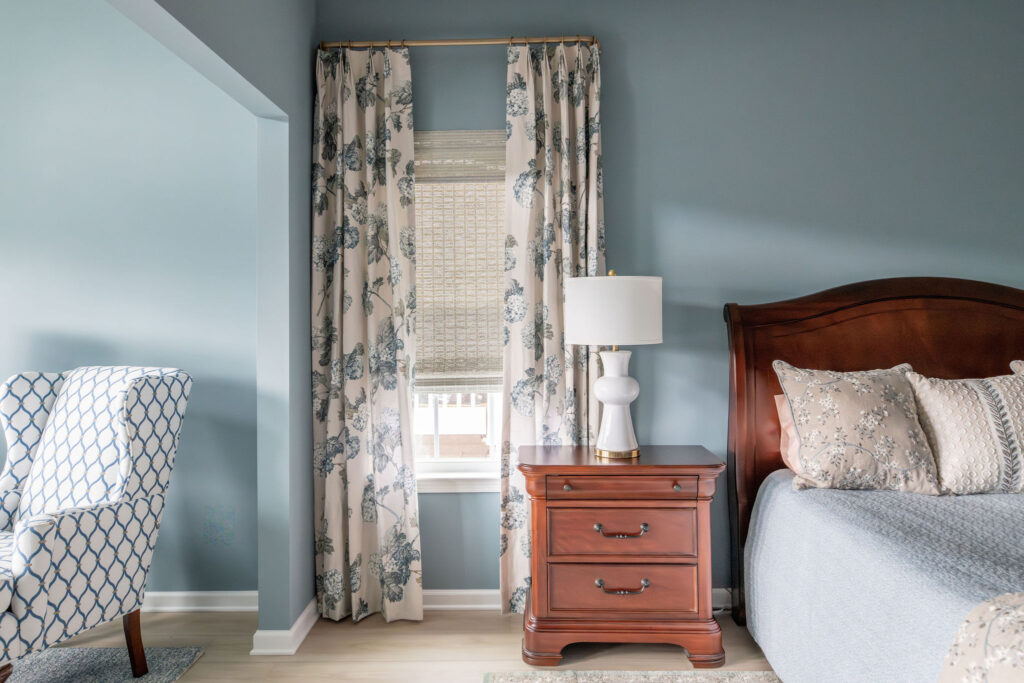 Master Bedroom in the Peninsula Ohio home with dark wooden furniture, light blue walls, and custom floral window treatments. Lindsey Putzier interior design