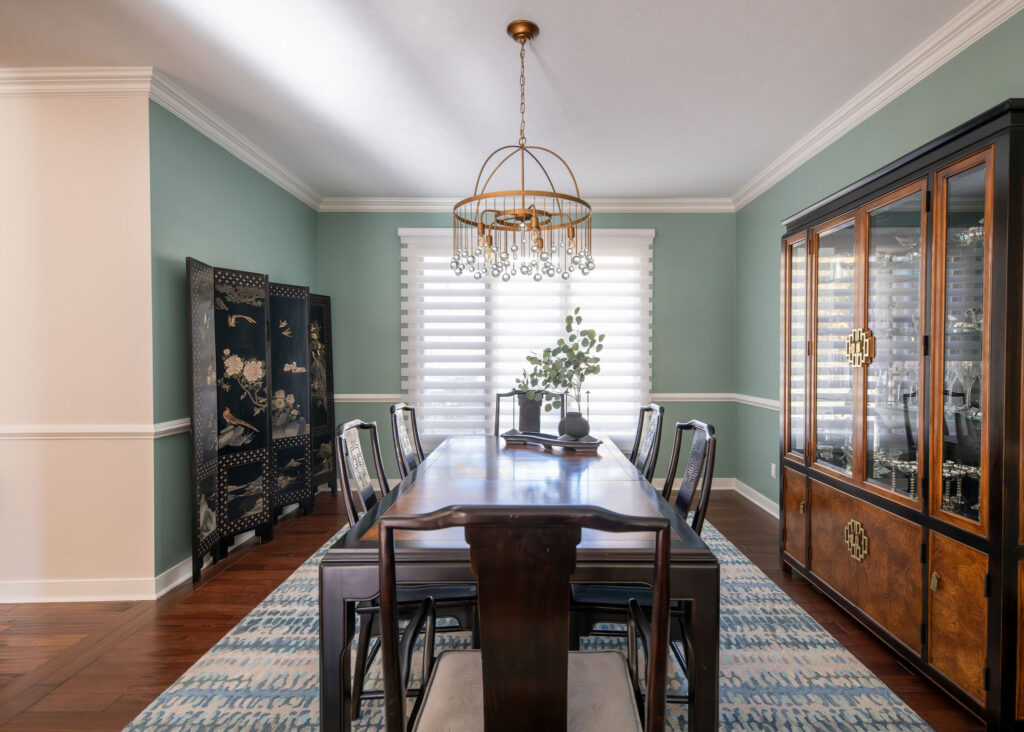 Dining room remodel in Chagrin Falls, Ohio with golden light fixture, green walls, and dark wooden furniture. Lindsey Putzier interior design