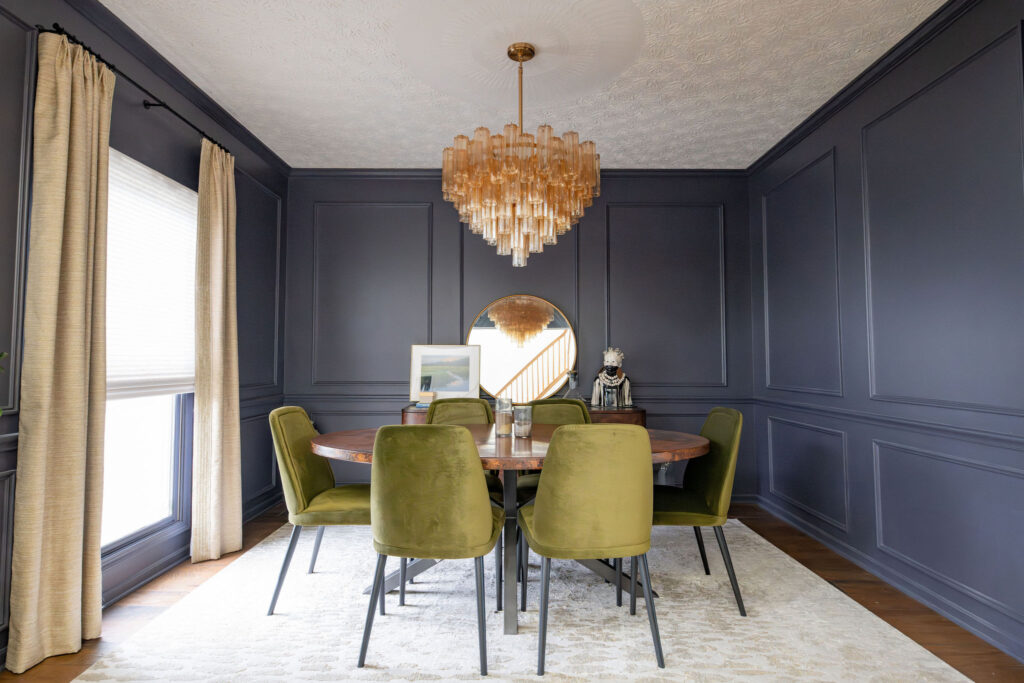 Formal dining room redesign with dark walls, hardwood flooring, large table with deep green upholstered chairs, large buffet, and custom window treatments. Lindsey Putzier interior design Copley Ohio