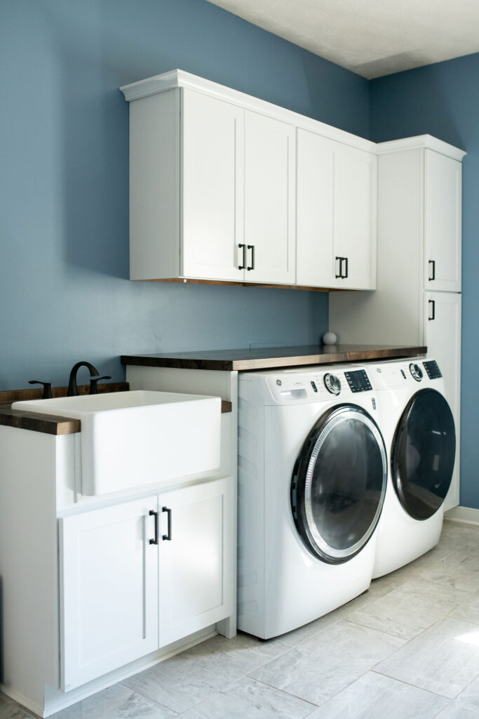 Laundry room integrated into the mudroom with wooden folding counter and white cabinets. Lindsey Putzier interior design