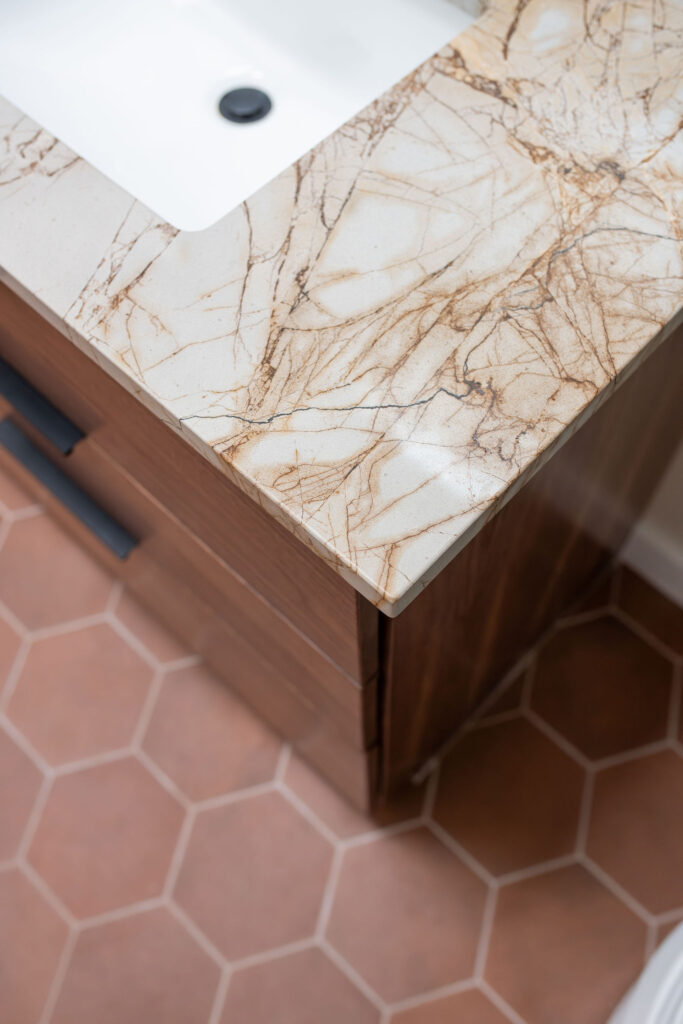 Master bathroom with rich marble countertops, terracotta hexagon tile flooring, and dark wooden vanity. Lindsey Putzier interior design Akron, Ohio