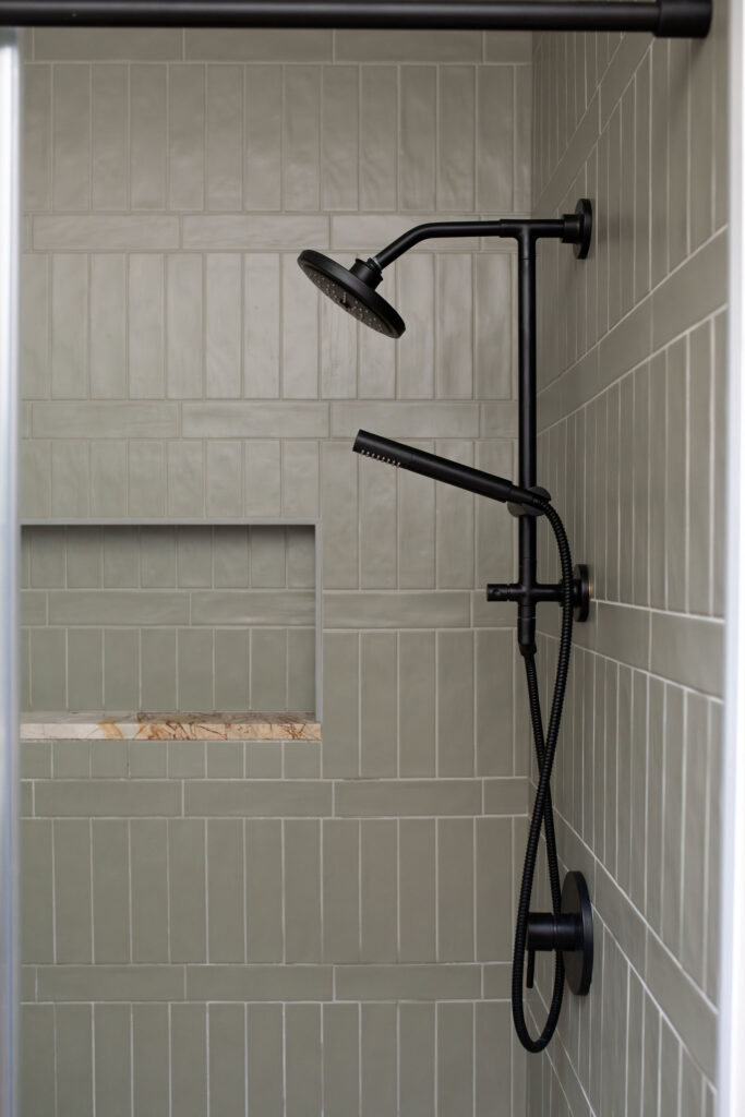 Green earthy tiled shower in the master bathroom of Akron Ohio home with black showerhead. Lindsey Putzier interior design