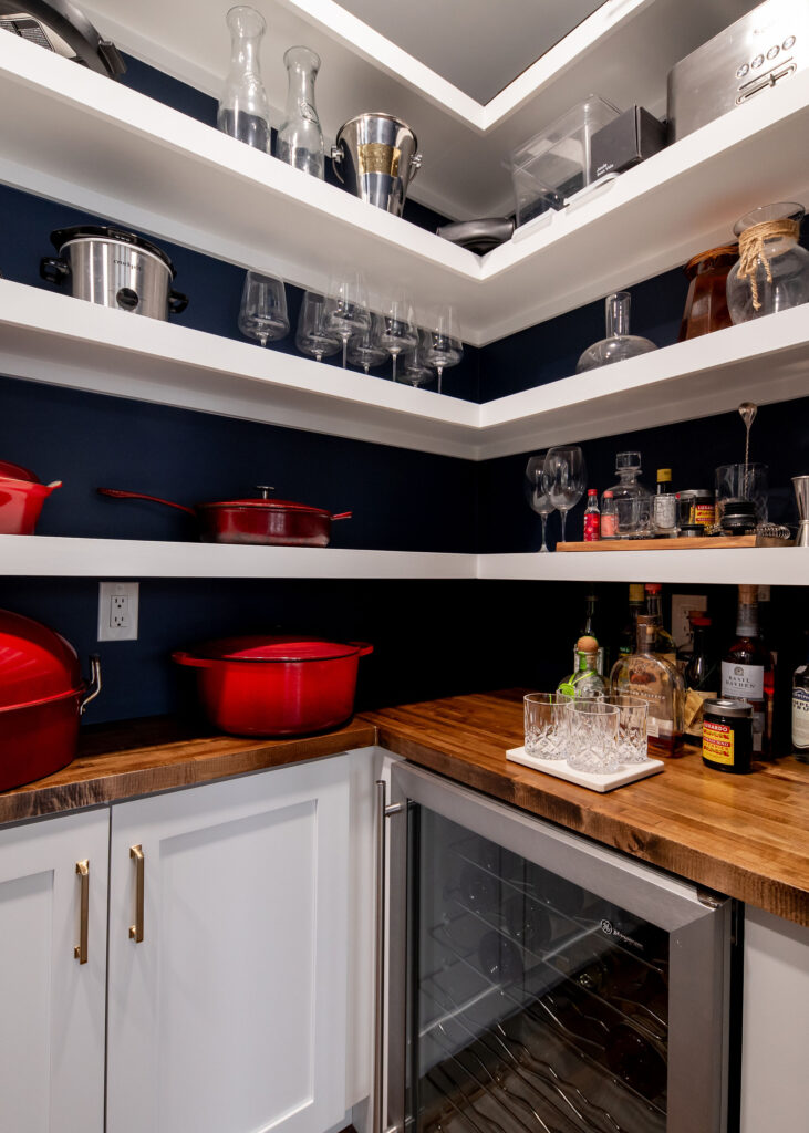 Butlers pantry with large open custom shelving in white, dark blue painted walls for contrast, butcher block countertops, and wine fridge. Lindsey Putzier interior design 
