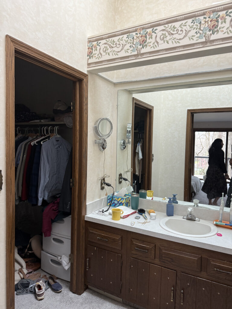 Before of the master bedroom with dated wallpaper, dark cabinetry, and laminate flooring. Lindsey Putzier interior design Akron Ohio 