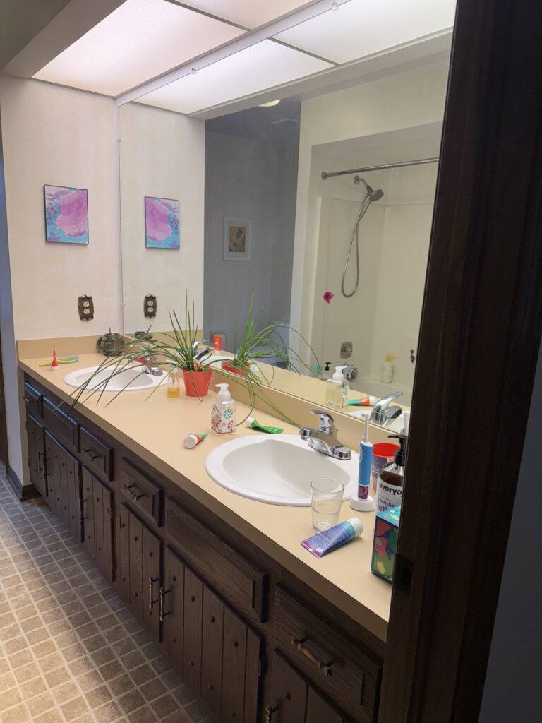 Before of the secondary bathroom with dated cabinetry, warm lighting and low ceilings. Akron Ohio interior design Lindsey Putzier 