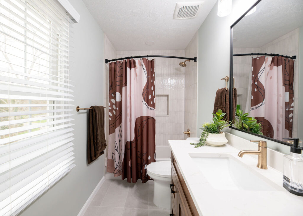 After of the Kids bathroom in Hudson Ohio with new tiled shower, updated wooden vanity and golden finishes. Lindsey Putzier interior design