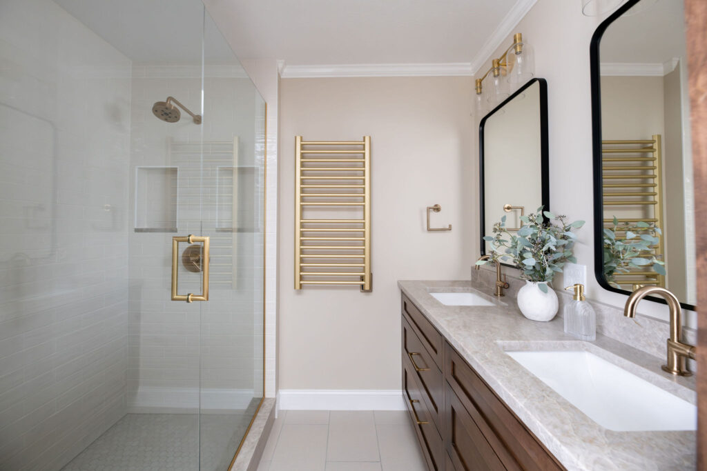 Master bathroom with deep wooden vanity, stone countertops, black trim mirrors, and a gold towel warmer. Lindsey Putzier interior deign Hudson Ohio