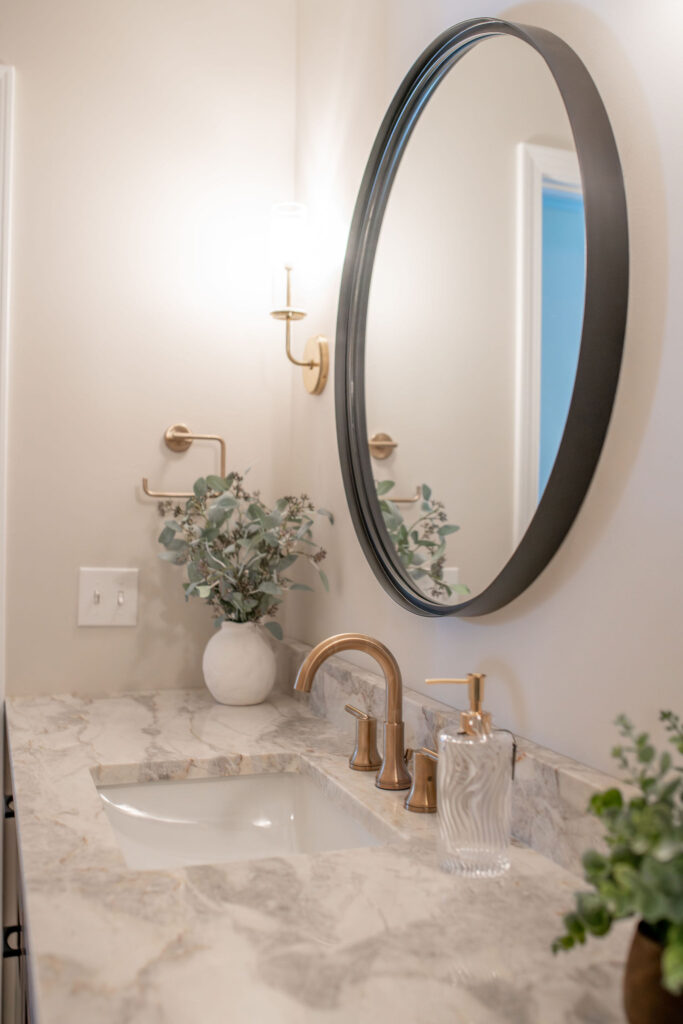 Powder room with marble countertops, gold faucet, golden sconces, and circle mirror. Lindsey Putzier interior design Hudson Ohio 