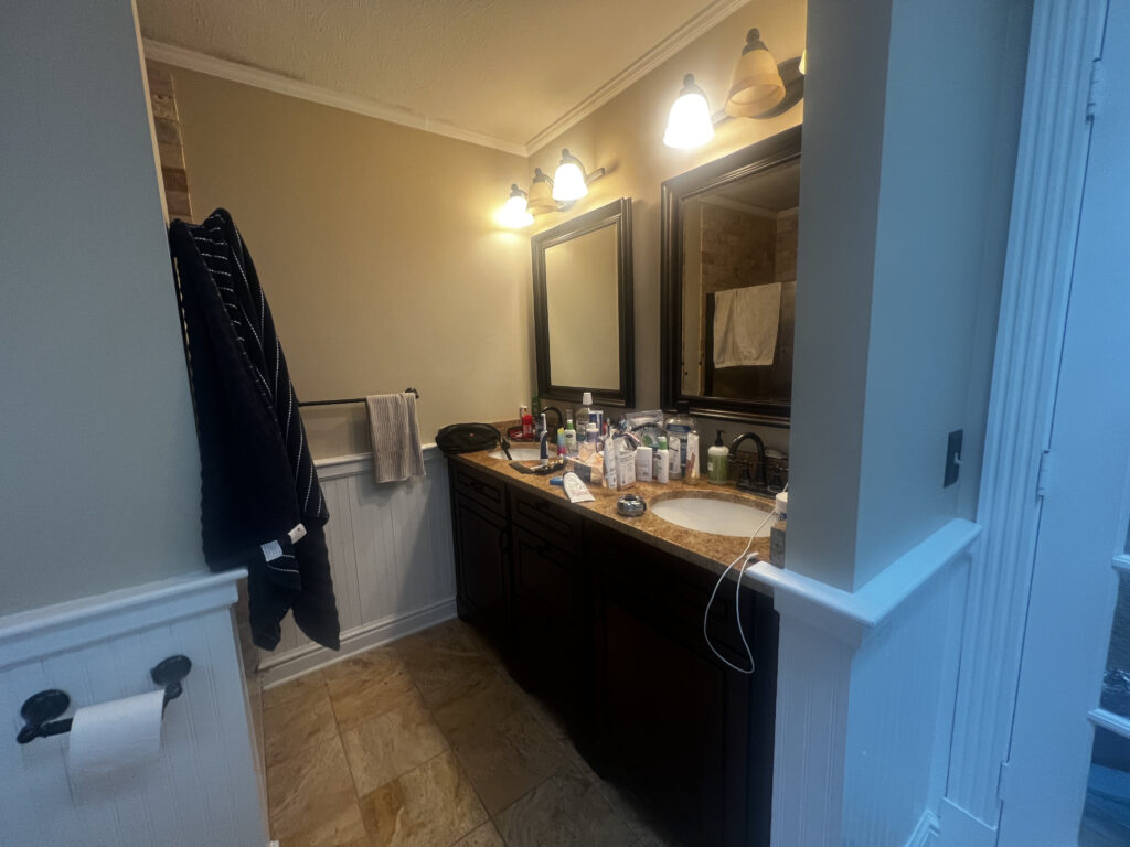 Before of the master bathroom with dark wooden cabinetry, warm countertops, and dated fixtures. Hudson Ohio interior design Lindsey Putzier 