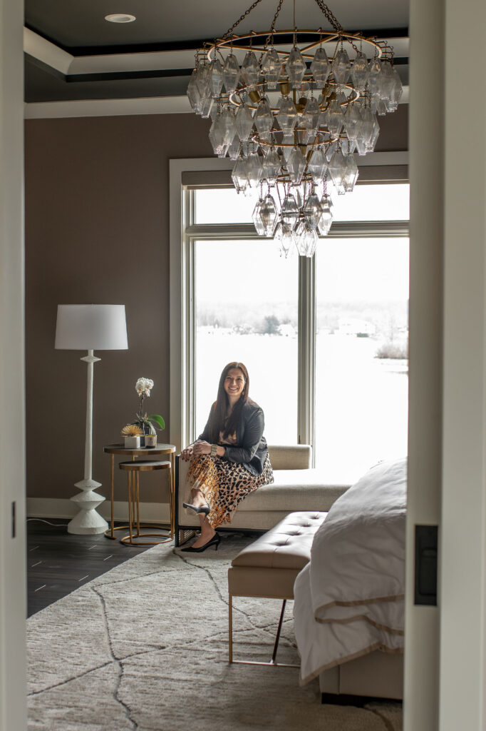 Lindsey Putzier, founder and principal designer, sitting in the master bedroom with large chandelier. Lindsey Putzier interior design Hudson Ohio