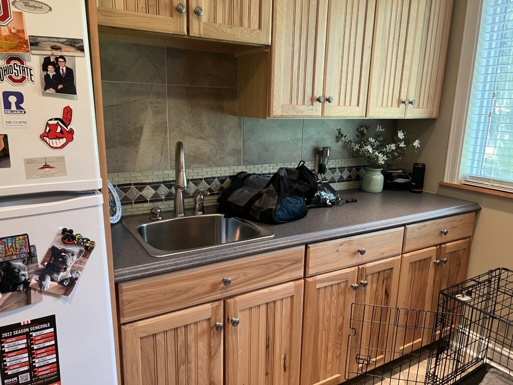 Before of the laundry room with dated backsplash and warm wooden cabinets. Hudson Ohio Interior design Lindsey Putzier
